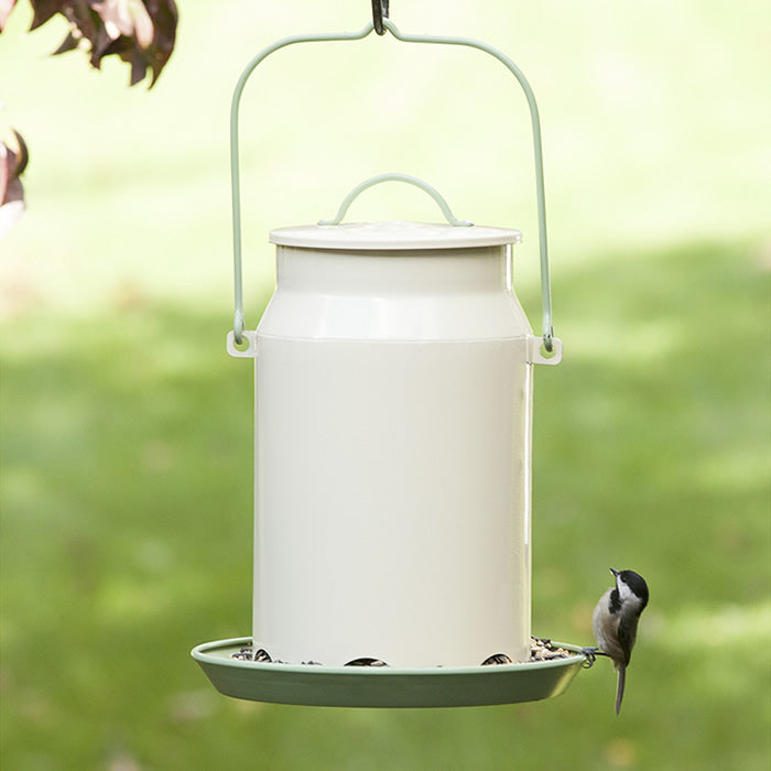 Milk Pail Bird Feeder with wraparound perch, filled with bird food, featuring six feeding ports and a decorative lid, attracting birds to the traditional outdoor feeder.