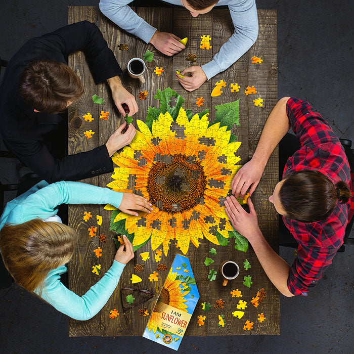 Group of people assembling the I Am Sunflower 350 pc. Puzzle, featuring a sunflower design and educational booklet with gardening tips.