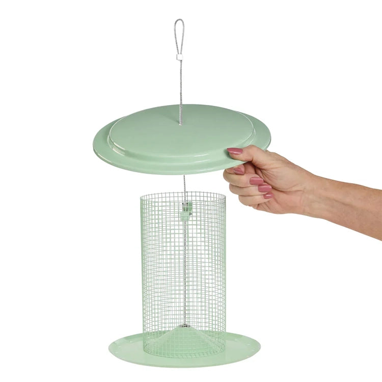 Hand lifting the lid of a sage green sunflower seed bird feeder for easy filling.