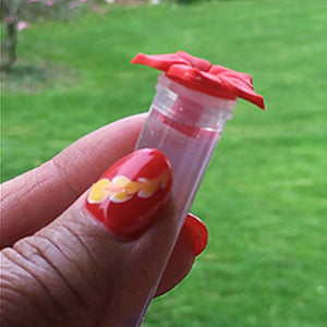 Hand holding the MINI HUM-fi™ Handheld Hummingbird Feeder, a small clear plastic tube with a red bow, designed for easy hand-feeding of hummingbirds.