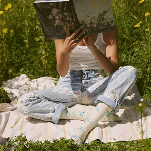 Person wearing blue hummingbird patterned socks while reading outdoors in a sunny garden