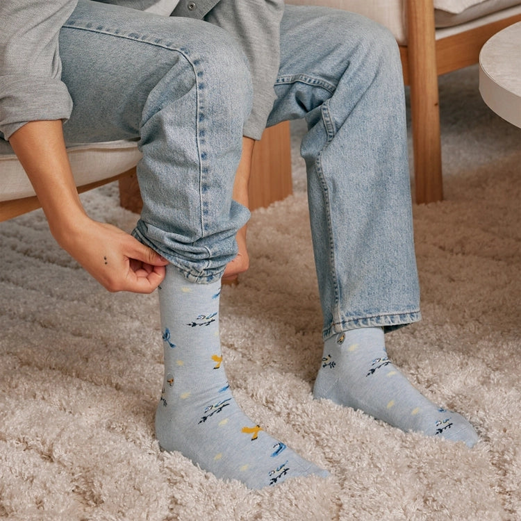Close-up of Conscious Step blue songbird socks being worn with jeans, featuring colorful birds in flight