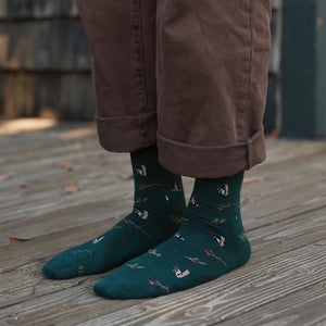 Person wearing forest green woodpecker socks with colorful bird and berry designs