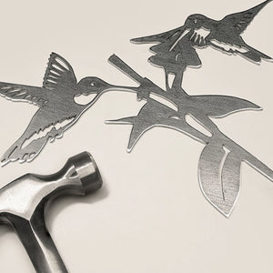 Hummingbird Honeys, Regular. A metal sculpture of hummingbirds crafted from Corten Steel, displayed with a hammer and nails on a white surface.