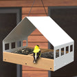 Nordic Habitat White Fly Thru Platform Feeder with a teak finish base. A yellow and black bird is perched, feeding on the chalet-style platform.