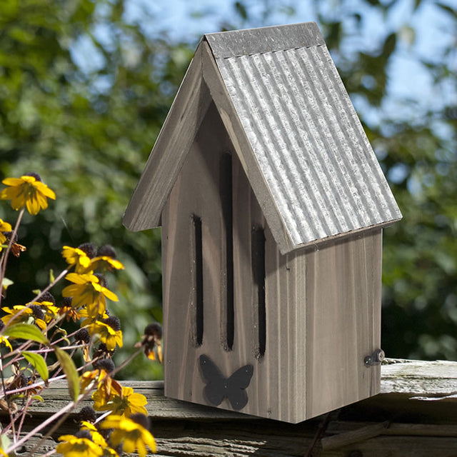 Rustic Farmhouse Butterfly House with slotted openings, mounted on a fence, featuring a galvanized metal roof and decorative butterfly accent in front.