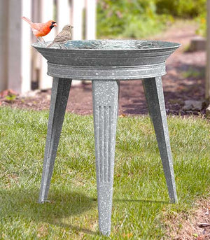 Vintage Galvanized Metal Bird Bath with embossed lines, standing on three legs. Features a bird perched on the rim of the metal basin.