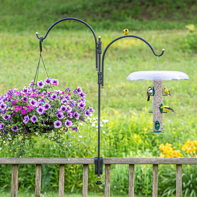 Platinum Cap Two Arm Clamp-On Deck Hanger with bird feeder and basket of flowers on a garden fence.