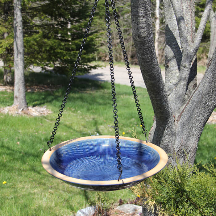 Hanging Radial Bird Bath, Baywater Blue, suspended from a tree with a 30-inch chain, showcasing a concentric circle design in a garden setting.