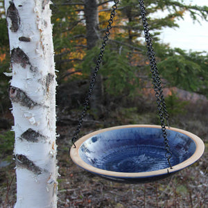 Hanging Radial Bird Bath, Baywater Blue, suspended from a tree, filled with water, showcasing the concentric circle design in a backyard setting.