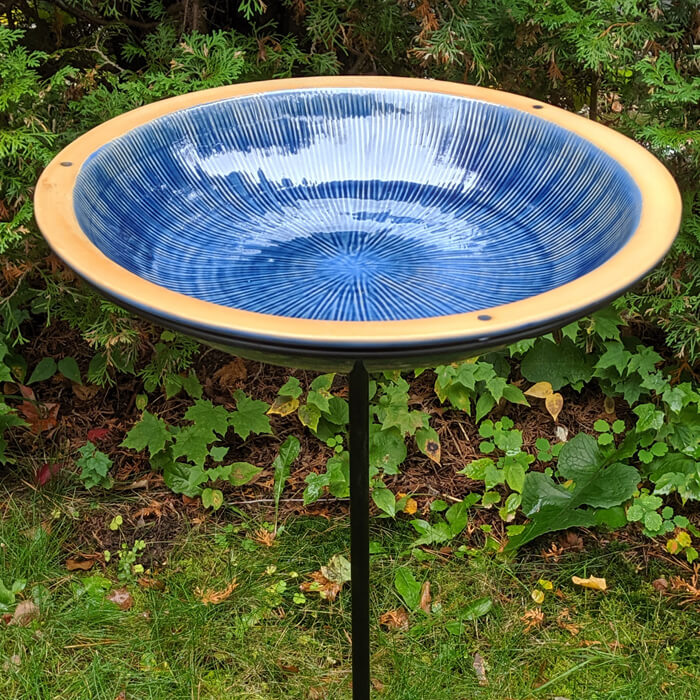 Post Radial Bird Bath, Baywater Blue, in a garden with a stoneware basin and a sturdy black steel pole with a three-pronged foot stake.