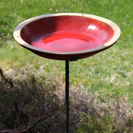 Post Radial Bird Bath, Autumn Red, in a grassy garden, featuring a 14-inch stoneware basin on a sturdy metal pole.