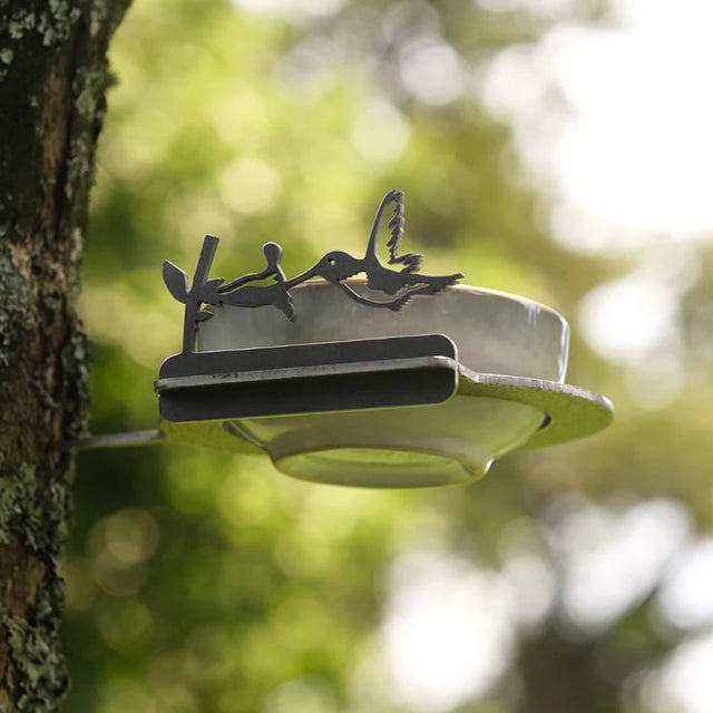 Metal Bowl Feeder Holder attached to a tree, designed to attract birds. Made of durable Corten Steel, it holds various vessels and develops a unique patina over time.