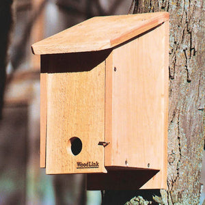 Cedar Winter Roosting Box mounted on a tree, featuring a 1-9/16 inch entry hole and a removable wooden ladder for birds to gather warmth.