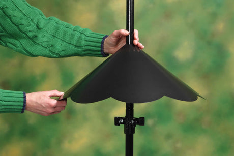 Person holding Extra Large Pole Baffle, Black, designed to prevent squirrels from reaching bird feeders.