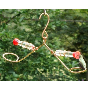 Tweeter Totter Hummer Feeder: A hummingbird on a copper feeder with glass tubes, perched on a circular swing, bobbing gently.