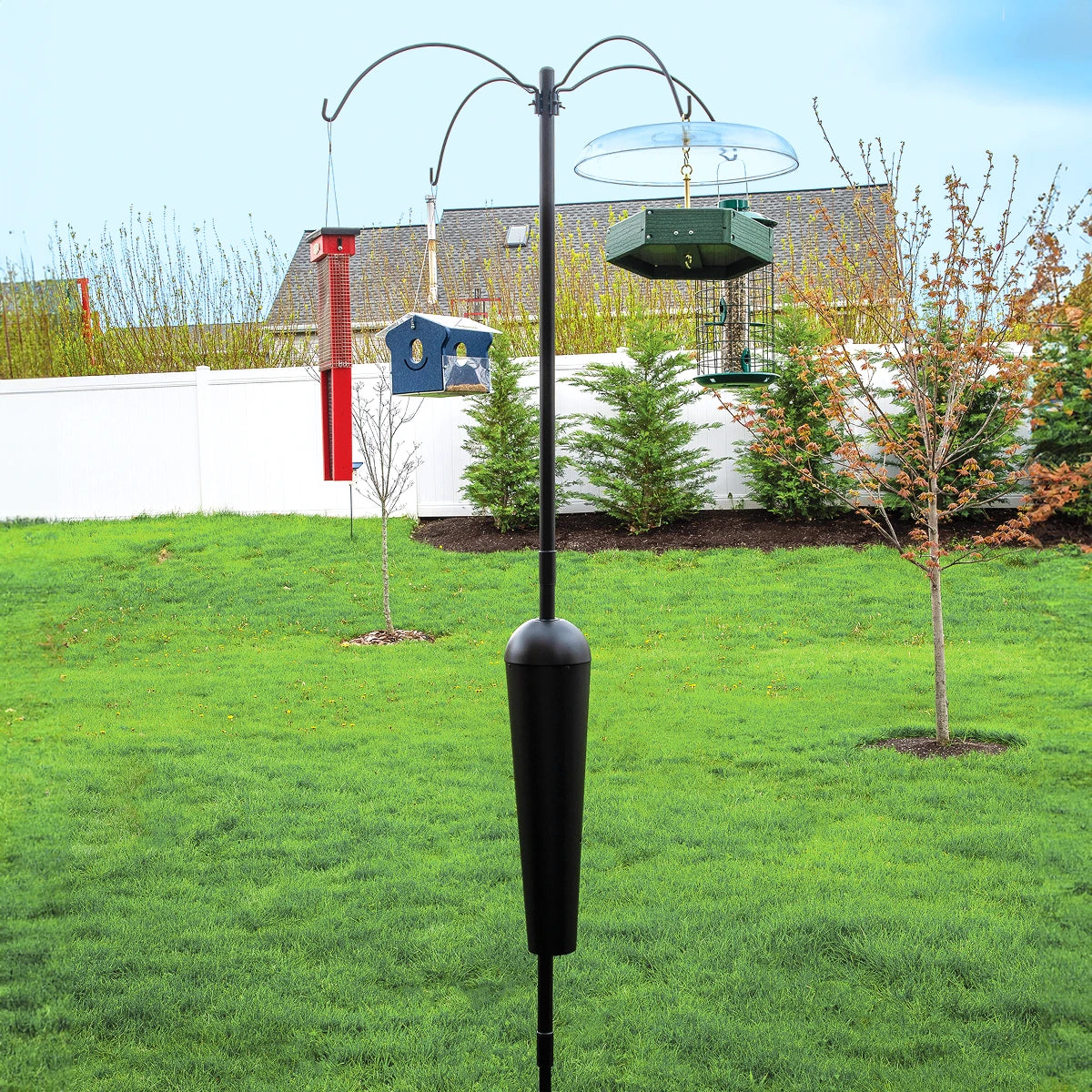 Squirrel Stopper Sequoia bird feeder station with four hangers on a sturdy black pole, featuring a squirrel-proof baffle, set in a grassy yard.