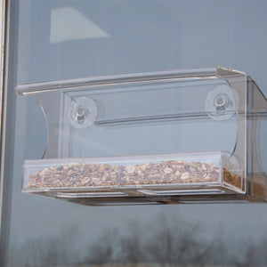 Window Bird Feeder with seeds, clear viewing areas, large roof, removable tray, curved rim, drainage holes, and heavy-duty suction cups for window attachment.