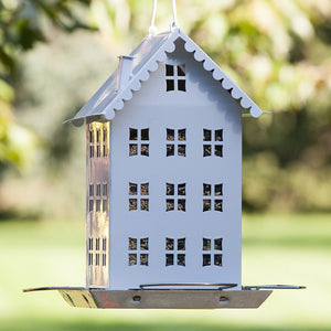 White Farmhouse Bird Feeder hanging from a tree, featuring a house-like design with four feeding ports and wide perches, ideal for attracting various birds.