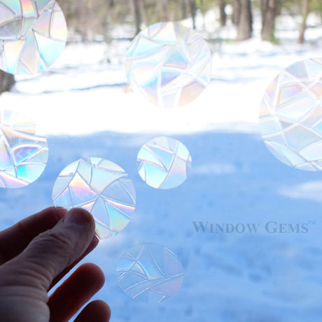 Hand holding a circular prismatic decal from the Dots Window Gems set of 15, designed to prevent bird collisions with windows.