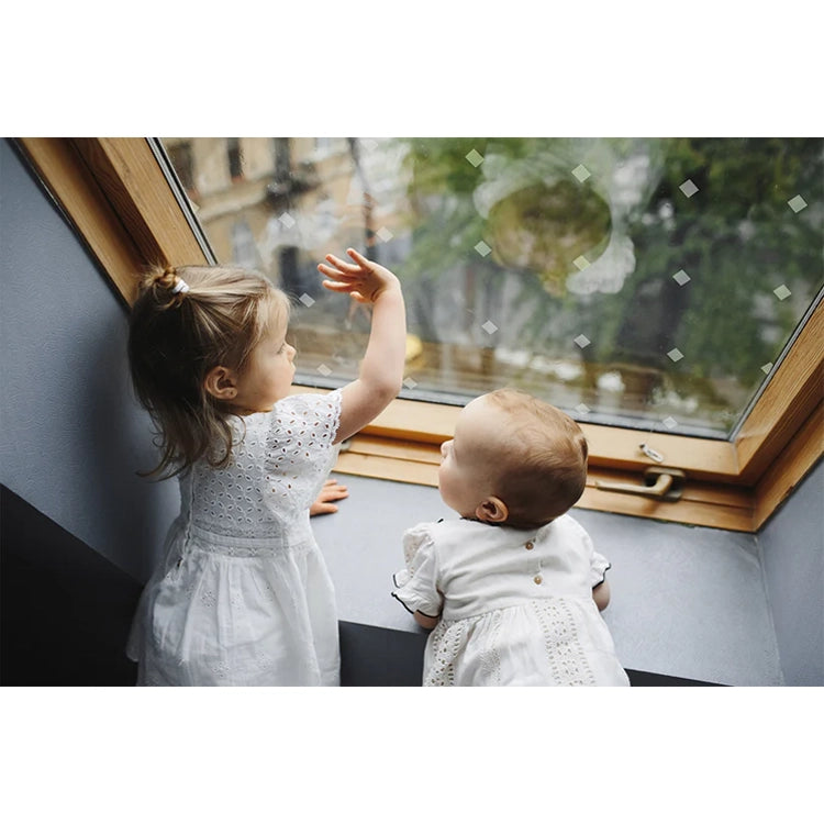 Two young children in white dresses looking out a window