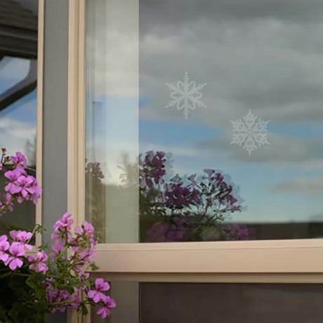 Snowflake WindowAlert Decals on a window with purple flowers, designed to prevent bird collisions by reflecting ultraviolet light.