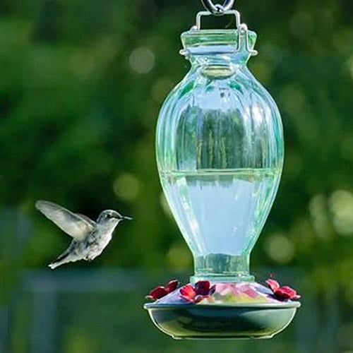 20 oz. Fluted Glass Hummingbird Feeder featuring a clear glass reservoir with colorful flower-shaped feeding ports and a metal hanger.