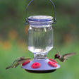 Lavender Field Top-Fill Glass Hummingbird Feeder with five red, zinnia-shaped feeding ports, clear glass jar, and easy-clean removable parts. Hummingbird feeding nearby.