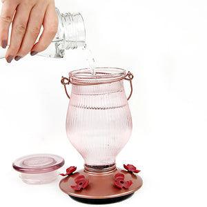 Hand pouring water into the Rose Gold Top-Fill Glass Hummingbird Feeder, showcasing its clear glass jar and wide mouth opening for easy filling.