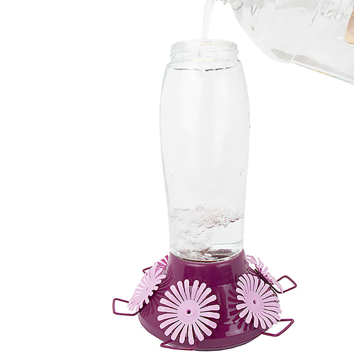 Person pouring water into Perky-Pet Top-Fill Hummer's Favorite Hummingbird Feeder, featuring a clear glass bottle and six flexible feeding ports, designed for easy filling and cleaning.