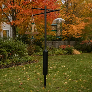 A black metal garden bird feeder stand with two hanging feeders, shown in a backyard lawn with autumn trees in the background.