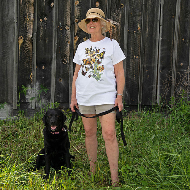 Butterflies of North America T-Shirt: Woman with sun hat standing beside a black dog in grass, holding a strap.