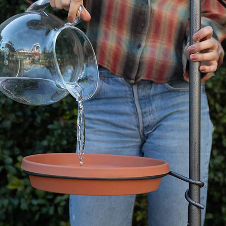 Person pouring water into a bird bath on the Yard Tree Bird Feeder Hanger, featuring customizable hooks and a sturdy, anti-tip design for outdoor use.