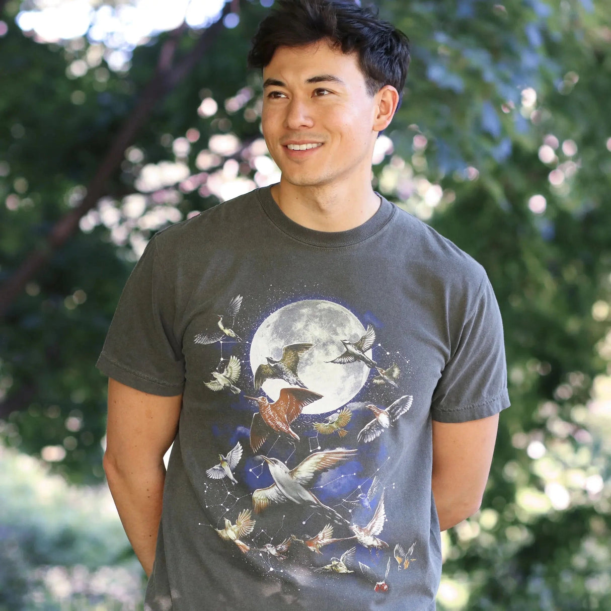 Man smiling, wearing a Bird Collective Night Migration Vintage T-Shirt, featuring birds flying with the moon, promoting bird conservation awareness.